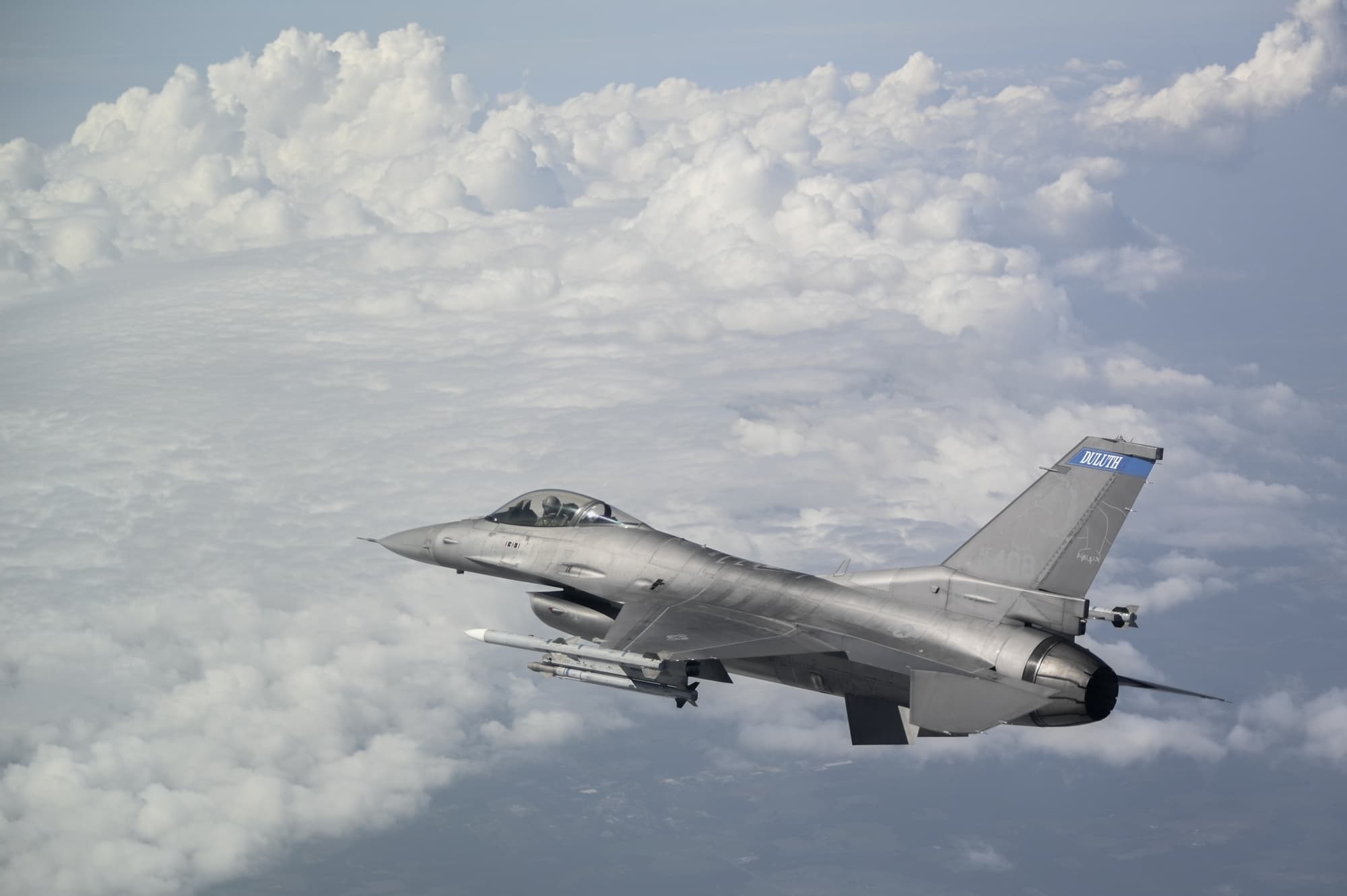 An Air Force F-16 flying above a layer of clouds